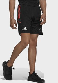 Svarta sportshorts med orange sidodetaljer och resårmidja. Har Adidas-logotypen och All Blacks-emblemet på vänster ben.