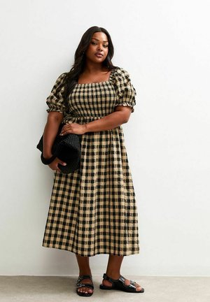 Vestido a cuadros en negro y beige con mangas cortas abullonadas, escote cuadrado y cintura ceñida. Combinado con un bolso negro texturizado y sandalias.