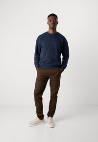 Navy sweatshirt, soft fabric, crew neck, minimal branding. Brown trousers, slim fit, cotton blend. Light beige sneakers, lace-up design.
