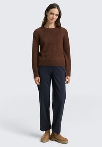 Brauner, strukturierter Strickpullover mit rundem Halsausschnitt, kombiniert mit navyblauen, weit geschnittenen Hosen und beigefarbenen Wildleder-Stiefeletten. Einfaches Design, lockere Passform.