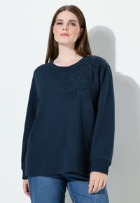 Sudadera de manga larga azul marino con un diseño de bordado floral texturizado en el hombro izquierdo. Hecha de tela suave para mayor comodidad.