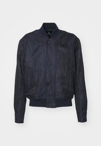 Veste bomber bleu foncé avec motif texturé subtil, fermeture à boutons, col, poignets et taille côtelés, présentée sur fond blanc.
