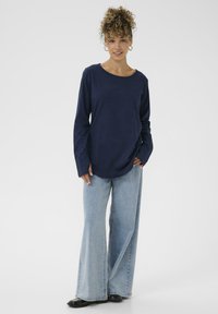 Maglietta a maniche lunghe blu navy in tessuto morbido, abbinata a jeans in denim a gamba larga di un blu chiaro. L'outfit presenta una vestibilità morbida e un design semplice.