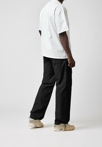 Weißes Baumwoll-T-Shirt mit kurzen Ärmeln, kombiniert mit schwarzen Cargo-Hosen. Die Schuhe haben Beigetöne mit Akzenten. Einfaches, funktionales Design.