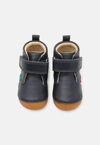 Kožené dětské boty v tmavě námořnické barvě, zdobené tan gumovou podrážkou, suchými zipy a měkkým béžovým podšívkou. Akcentové štítky v zelené a červené barvě.