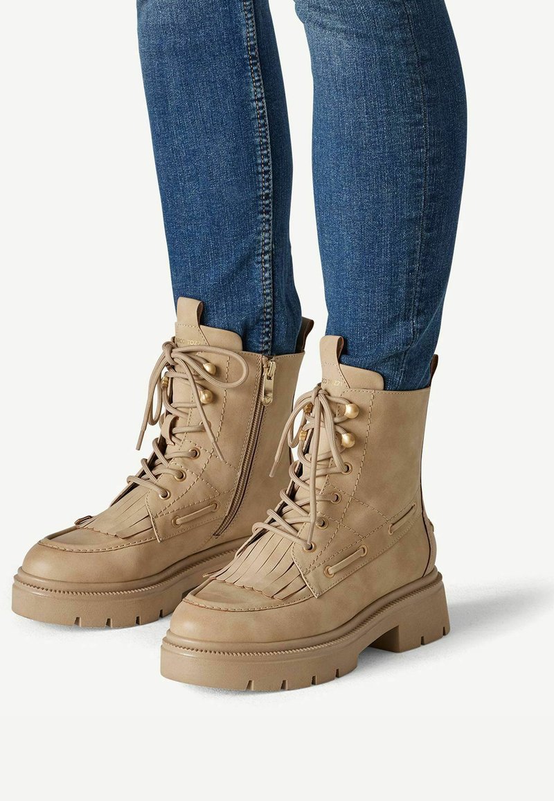 Bottines lacées couleur camel avec fermeture éclair latérale et détail à franges, portées avec un jean bleu ajusté.