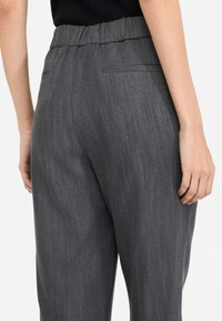 Pantaloni grigi con un tessuto strutturato, vita elasticizzata e due tasche posteriori. Il design presenta una vestibilità rilassata e linee pulite.