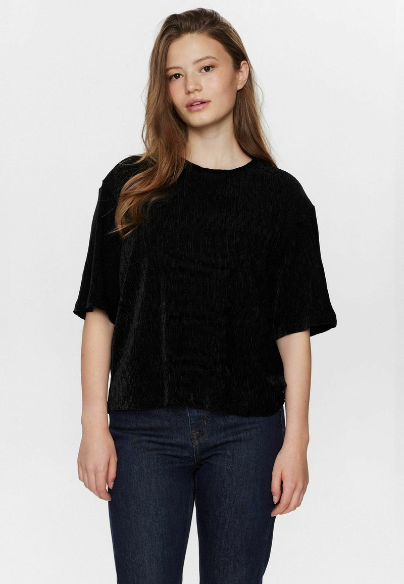 Svart, kortärmad topp i texturerad tyg med lös passform och rundad halsringning, tillsammans med mörka jeans på en enkel bakgrund.