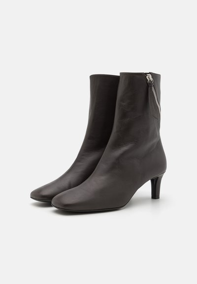 Svarta läderankelstövlar med en elegant design, spetsig tå och dragkedja på sidan. Klacken har en blygsam höjd, cirka 6,5 cm.