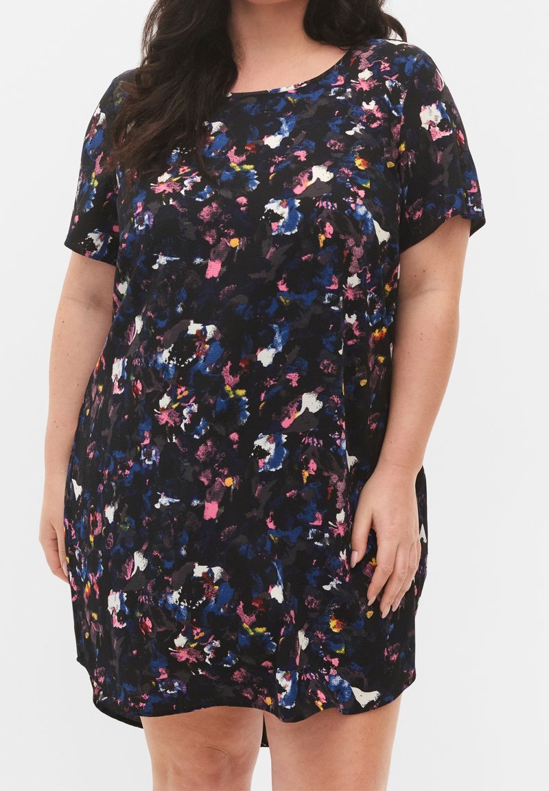Femme portant une robe à manches courtes, longueur genoux, avec un motif floral abstrait coloré sur fond noir.