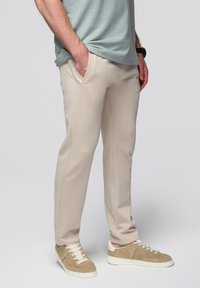 Lichtbeige joggingbroek gemaakt van zachte stof, met zijzakken en een tapered ontwerp. Draagt bij neutraal gekleurde sneakers.