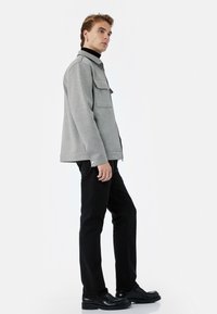 Szara, teksturowana kurtka z kołnierzem i dwiema przednimi kieszeniami, w zestawieniu z czarnymi spodniami i czarnymi botkami. Czyste linie, minimalistsyczny design.