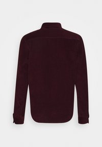 Burgundy kordflorskjorta med långa ärmar, knäppbar krage och böjd nederkant. Har ribbad textur och knappade manschetter.