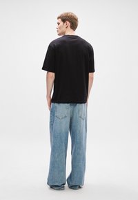 Μαύρη βαμβακερή μπλούζα T-shirt με χαλαρή εφαρμογή, σε συνδυασμό με ανοιχτό μπλε τζιν παντελόνι με φαρδιά πόδια, που διαθέτει πέντε τσέπες και διακριτές ραφές.
