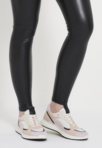 Sneaker leggera che presenta un mix di materiali rosa soft, bianco e beige, con pannelli in rete, dettagli testurizzati e un bordo nero a contrasto.