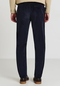 Pantaloni di velluto a coste blu navy con una texture sottile, taglio dritto e tasche posteriori, abbinati a scarpe marroni scure.