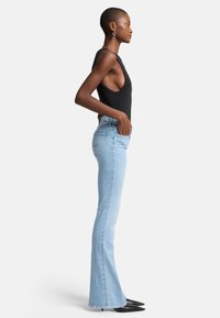 Jeans flare di un blu chiaro con tasche frontali, vita media e cuciture a contrasto, abbinati a un top fitted nero e tacchi neri.