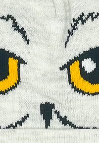 Witte gebreide beanie met een ontwerp van zwarte en gele uilenogen. Textuurstof met duidelijke stikdetails.