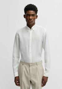 Witte linnen overhemd met lange mouwen en een button-down kraag, subtiele textuur, gecombineerd met beige geklede broek met textuur.