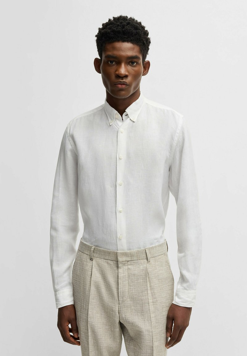 Witte linnen overhemd met lange mouwen en een button-down kraag, subtiele textuur, gecombineerd met beige geklede broek met textuur.