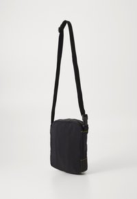 Svart crossbody-väska med rektangulär form, tillverkad av texturerad tyg, har gula sömmar, dragkedjestängning och en justerbar rem.