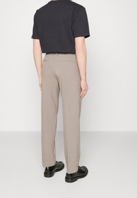 Tmavě šedá košile s krátkým rukávem spárovaná se světle béžovými kalhotami. Kalhoty mají rovný střih a dva zadní kapsy. Černé boty dokončují vzhled.