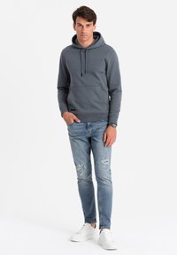 Grijze hoodie met een kangoeroezak, capuchon met trekkoord en geribde manchetten; gecombineerd met lichtblauwe versleten jeans en witte sneakers.