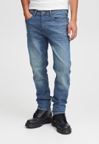 Mėlyni džinsai iš džinso medžiagos, aptempto silueto, su penkiomis kišenėmis ir pašviesintomis detalėmis. Derinami su juodais auluotais batais su masyviu padu.