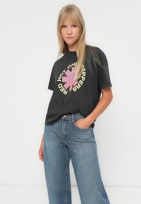 Črna bombažna majica s pisanimi grafikami "Red Hot Chili Peppers" spredaj, v kombinaciji s svetloblue denim kavbojkami.
