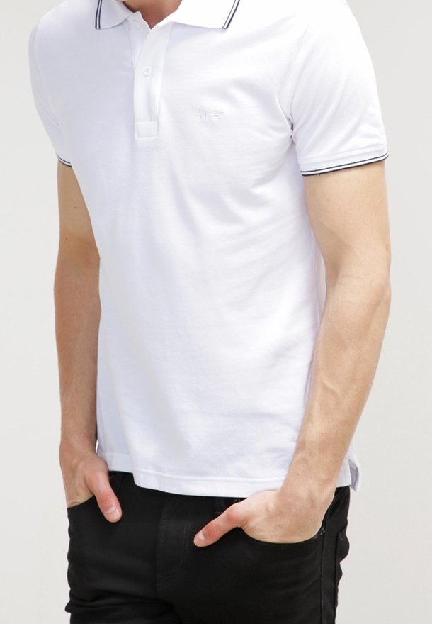 Chemise polo blanche avec un col à deux boutons et des accents rayés noirs sur le col et les manches. Portée avec un pantalon noir, affichant une texture uniforme.