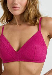 Bralette en dentelle fuchsia avec un design en V et des bretelles ajustables, présentant une texture à motif floral et une bande lisse pour le confort.