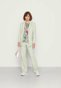 Blazer verde claro e calças combinando, feitas de um tecido suave. Por baixo, uma camisa com padrão floral em cores suaves. Bolsa rosa clara.