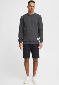 Donkergrijze sweatshirt met geribde boorden en zoom, gecombineerd met zwarte shorts. Model draagt witte sneakers. Eenvoudig, casual ontwerp met een klein label.