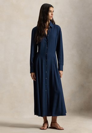 Tmavomodré šaty na zapínanie s dlhými rukávmi, golierom a rozšírenou sukňou s dĺžkou do kolien, vyrobené z hladkej látky.