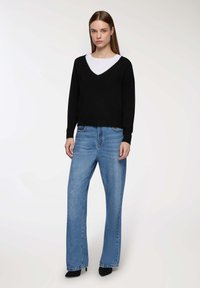Maglione nero a scollo a V abbinato a jeans a gamba larga di colore azzurro chiaro. L'outfit presenta un taglio casual, con una texture liscia e colori a contrasto.