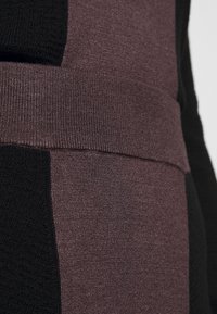 Lähikuva neulotusta kankaasta mustista ja tumman violetista värilohkoista sekä tekstuurillisesta vaakasaumasta.