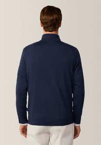 Pull en maille bleu marine avec un col, des manches longues et des poignets côtelés. Texture douce, coupe ajustée et détails de design minimalistes.
