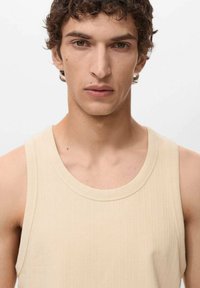 Top beige a canottiera con una texture a costine e scollo ampio, caratterizzato da linee pulite e dettagli minimi, realizzato in un materiale morbido.