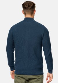Jersey de color azul marino con cuello alto, mangas largas y puños acanalados. Presenta un patrón tejido texturizado y un dobladillo recto.