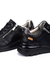 Schwarze Ledersneaker mit strukturiertem Finish, ausgestattet mit einem seitlichen Reißverschluss, Schnürverschluss und einem kontrastierenden, braunen Etikett an der Ferse. Schlankes, rundes Design.