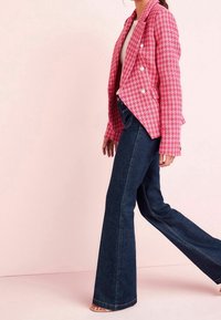 Pink houndstooth blazer with double-breasted buttons, paired with dark blue flared jeans featuring visible stitching and a smooth texture.