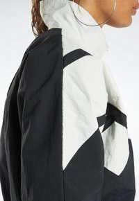 Svart och vit högkragad jacka med geometrisk färgblockering, slät textur och dragkedjedetaljer längs framsidan och axlarna.