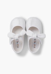 White baby shoes with perforated design, rounded toe, and white fabric bow detail. Inside features a soft lining and logo tag.