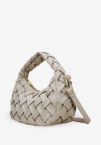 Bolso tejido en color beige con una silueta curva, que cuenta con un asa superior y una correa de hombro desmontable. El cierre cuenta con detalles en oro.
