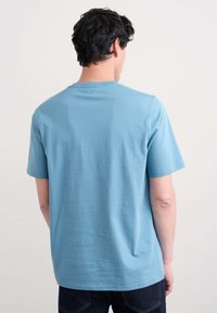 Camiseta de algodón azul claro con cuello redondo y mangas cortas, que presenta una textura suave y un corte relajado. Sin patrones ni gráficos visibles.