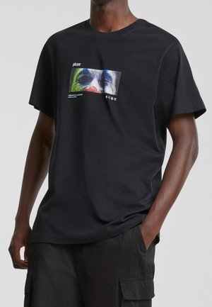 Schwarzes Baumwoll-T-Shirt mit einem farbenfrohen Grafikdruck eines Gesichts, einem rechteckigen Design und Text, kurzen Ärmeln und einem lockeren Schnitt.