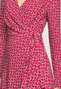 Czerwona sukienka w stylu kopertowym z długimi rękawami, wzorem łańcucha w białym i szarym kolorze, z wiązaniem w talii i miękką, gładką teksturą materiału.