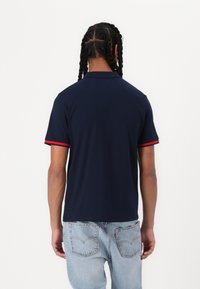 Navy polo shirt with red accent stripes on sleeves, made of smooth fabric, featuring a classic collar and short sleeves.