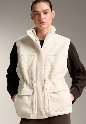 Cremfarbener Fleece-Weste mit hohem Kragen, Reißverschluss vorne und verstellbarem Kordelzug in der Taille. Verfügt über zwei Fronttaschen mit Klappenverschlüssen.