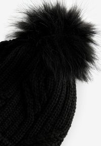 Schwarze Strickmütze mit strukturiertem Muster und einem großen schwarzen Kunstfellpompon oben. Weiches und warmes Material, geeignet für kaltes Wetter.